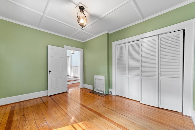 unfurnished bedroom with a closet, crown molding, coffered ceiling, and hardwood / wood-style flooring