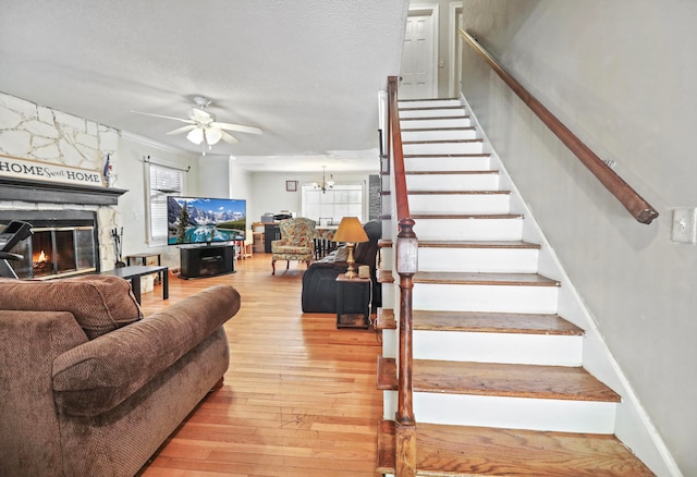 living room with wood-type flooring, a stone fireplace, ceiling fan with notable chandelier, and a healthy amount of sunlight