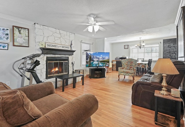 living room with light wood-type flooring, a textured ceiling, a stone fireplace, and ornamental molding