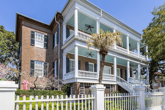 greek revival inspired property featuring ceiling fan, brick siding, a fenced front yard, and a porch