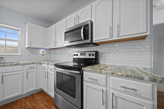 kitchen featuring white cabinets, appliances with stainless steel finishes, light stone counters, dark wood-type flooring, and backsplash