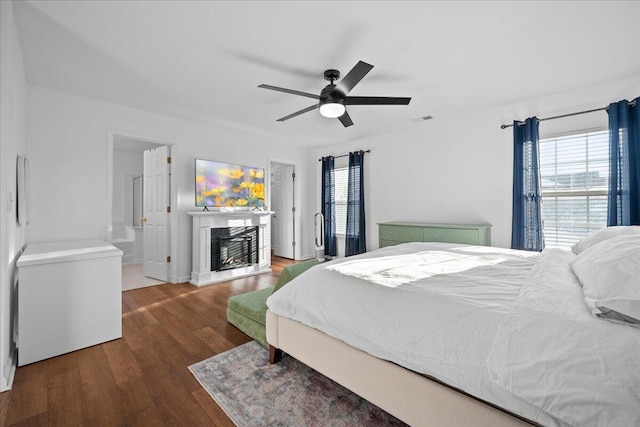 bedroom featuring refrigerator, a fireplace with raised hearth, visible vents, a ceiling fan, and wood finished floors
