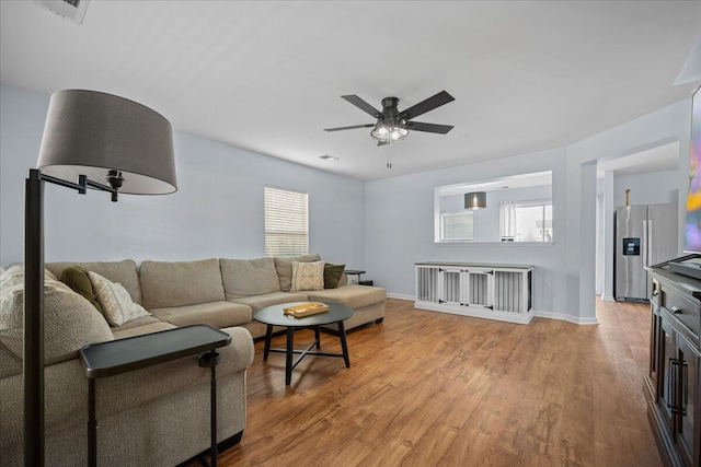 living room featuring a ceiling fan, baseboards, and light wood finished floors