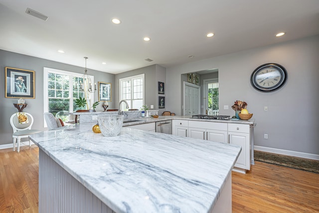 kitchen with hanging light fixtures, white cabinetry, light stone counters, light wood-type flooring, and sink