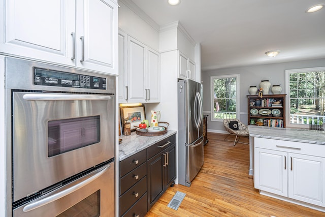 kitchen with light stone counters, white cabinetry, stainless steel appliances, crown molding, and light hardwood / wood-style floors