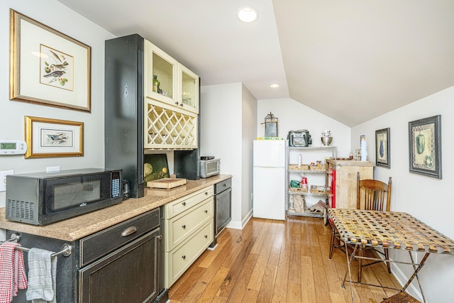 kitchen with cream cabinetry, lofted ceiling, light hardwood / wood-style flooring, and white fridge