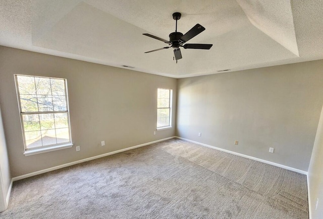 carpeted spare room featuring a raised ceiling, ceiling fan, and a textured ceiling