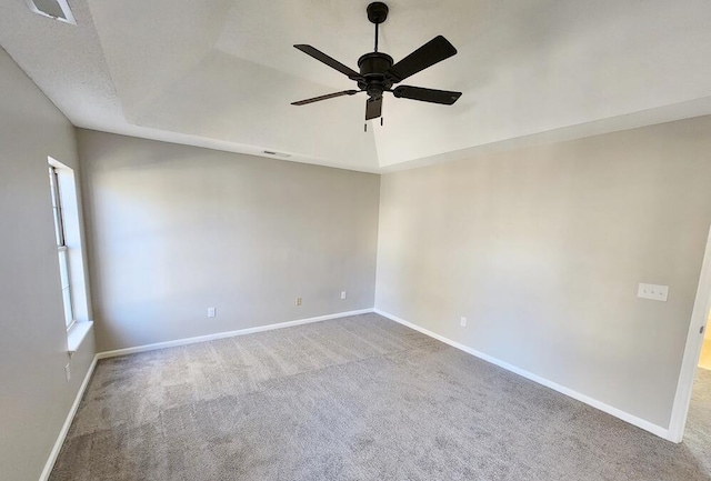 empty room featuring a raised ceiling, ceiling fan, light colored carpet, and a textured ceiling