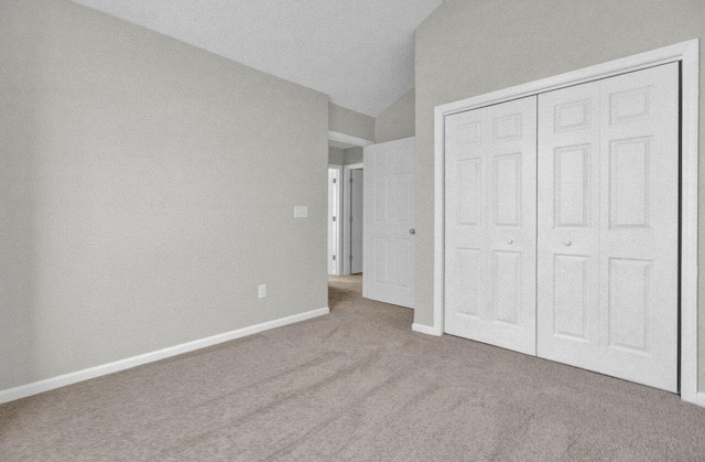 unfurnished bedroom with light colored carpet, lofted ceiling, and a closet