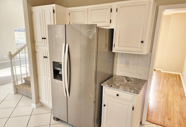 kitchen featuring stainless steel fridge with ice dispenser, decorative backsplash, light tile patterned floors, stone countertops, and white cabinetry