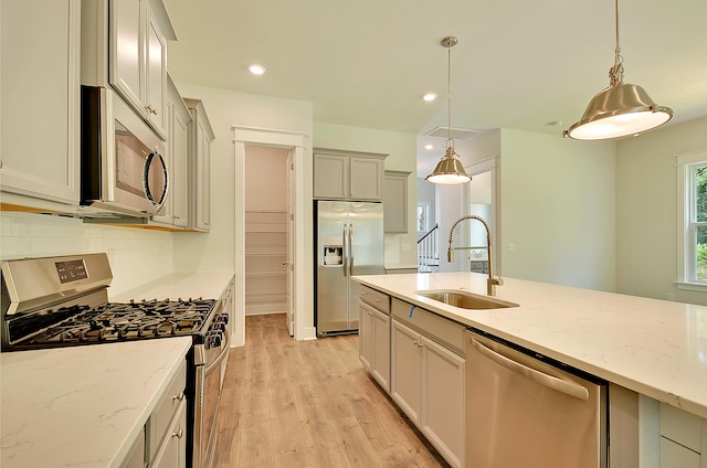 kitchen with decorative light fixtures, a sink, light stone counters, stainless steel appliances, and light wood-style flooring