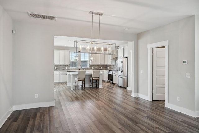 kitchen featuring stainless steel appliances, a breakfast bar, tasteful backsplash, dark wood-type flooring, and white cabinetry
