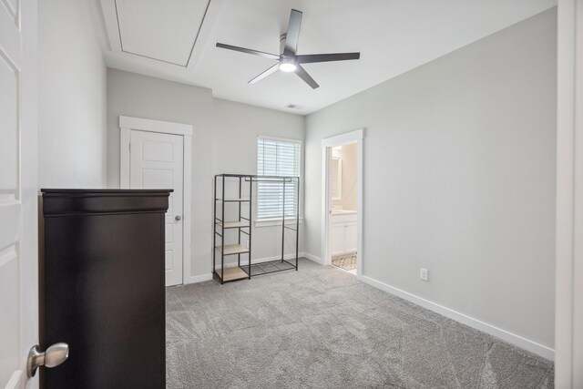 unfurnished bedroom featuring carpet floors, attic access, baseboards, connected bathroom, and ceiling fan