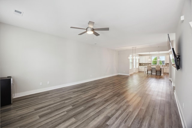 unfurnished living room with wood finished floors, baseboards, a ceiling fan, and a chandelier