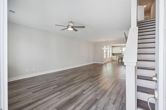 unfurnished living room with a ceiling fan, stairs, wood finished floors, baseboards, and a chandelier
