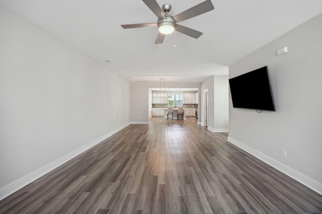 unfurnished living room featuring dark wood-style floors, a ceiling fan, and baseboards