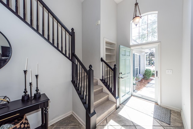 entryway featuring stairway, baseboards, a towering ceiling, and stone finish flooring