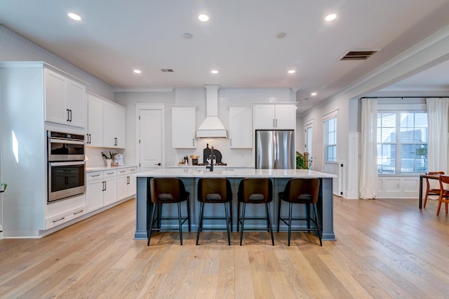 kitchen featuring white cabinetry, a center island with sink, stainless steel appliances, and premium range hood