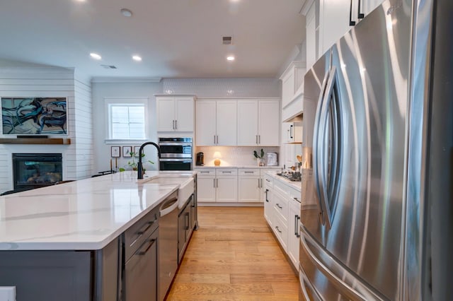 kitchen with appliances with stainless steel finishes, white cabinetry, a fireplace, light stone countertops, and an island with sink