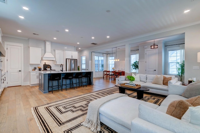 living room featuring light hardwood / wood-style flooring, sink, crown molding, and plenty of natural light