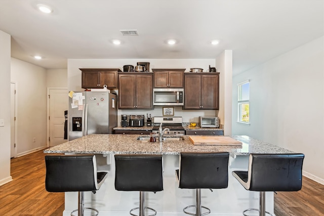 kitchen with a sink, a kitchen island with sink, stainless steel appliances, dark wood-type flooring, and visible vents