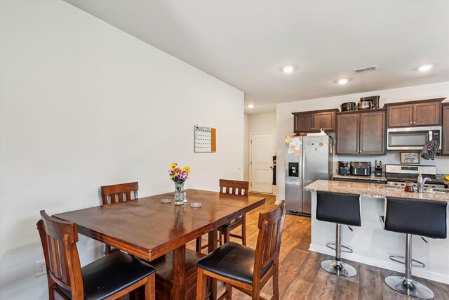 kitchen with stainless steel appliances, visible vents, dark brown cabinetry, a kitchen bar, and wood finished floors