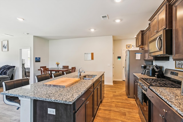 kitchen with light wood finished floors, a kitchen breakfast bar, stainless steel appliances, visible vents, and a sink