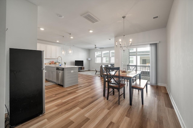 dining space with sink, ceiling fan with notable chandelier, and light hardwood / wood-style flooring