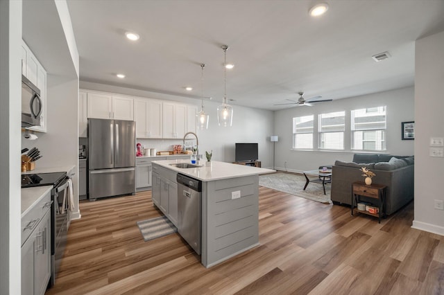 kitchen with white cabinets, appliances with stainless steel finishes, light hardwood / wood-style flooring, hanging light fixtures, and a center island with sink