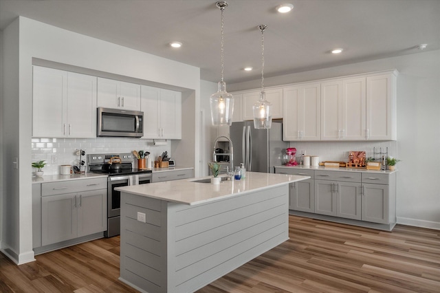 kitchen with appliances with stainless steel finishes, hanging light fixtures, a kitchen island with sink, gray cabinetry, and sink