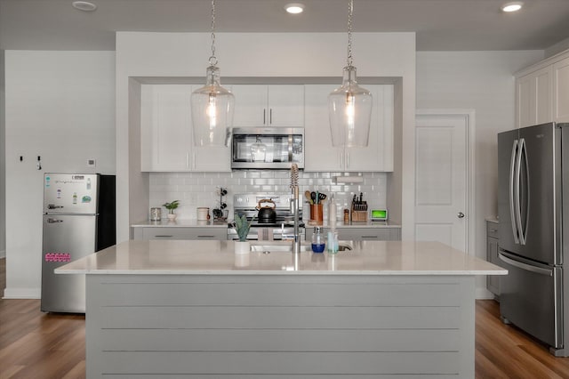 kitchen with white cabinetry, hanging light fixtures, a center island with sink, and appliances with stainless steel finishes