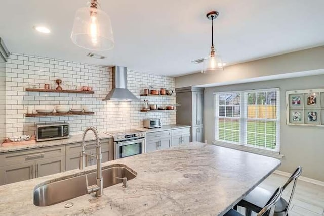kitchen with stainless steel appliances, open shelves, a sink, wall chimney exhaust hood, and baseboards
