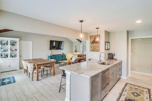 kitchen featuring dishwasher, a sink, a kitchen breakfast bar, hanging light fixtures, and light wood finished floors