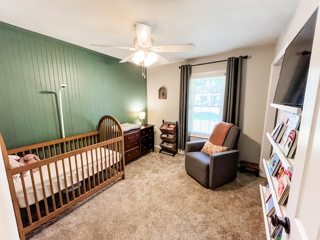 bedroom featuring light carpet, a crib, and a ceiling fan
