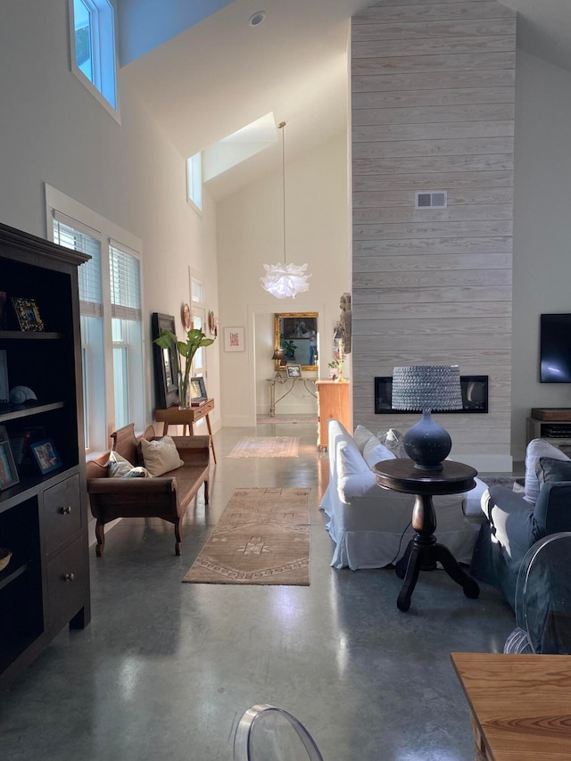 living room featuring concrete flooring, a fireplace, a high ceiling, and a chandelier