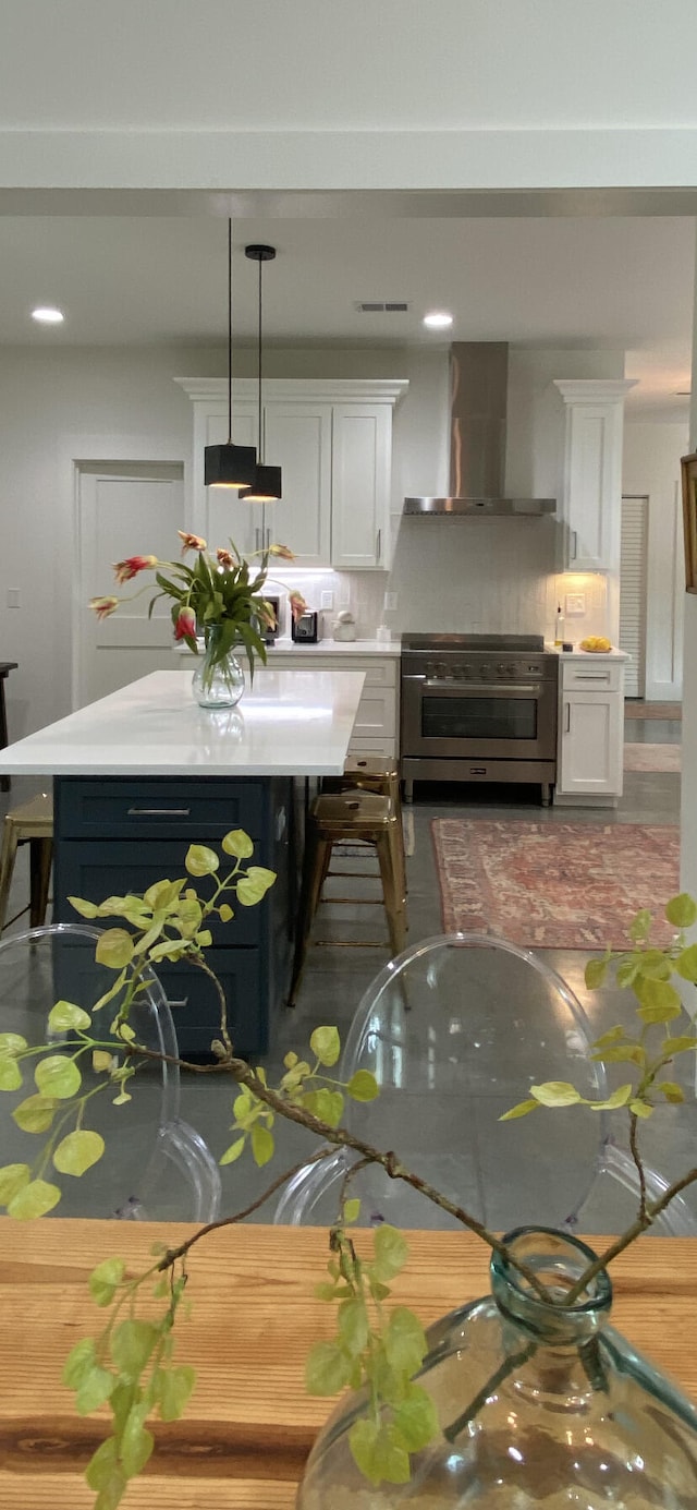 kitchen with decorative backsplash, stainless steel range, wall chimney range hood, white cabinetry, and hanging light fixtures