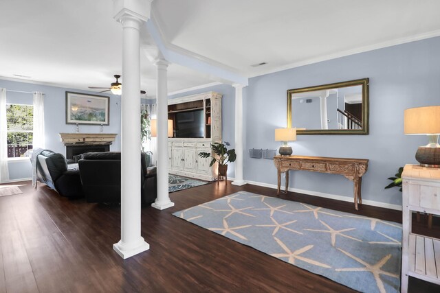 living area with baseboards, a ceiling fan, a fireplace, ornate columns, and wood finished floors