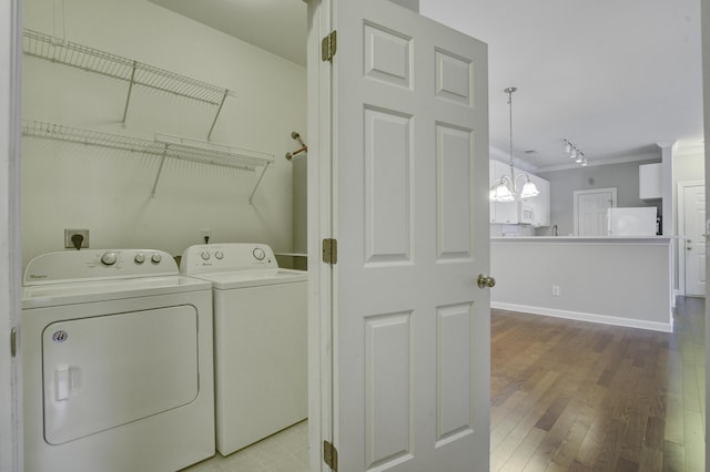 laundry room featuring crown molding, washer and clothes dryer, light hardwood / wood-style floors, and a notable chandelier