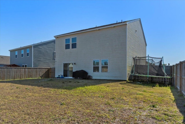 rear view of house with a yard, a trampoline, and a fenced backyard