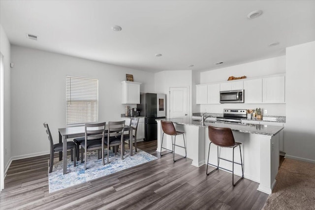 kitchen featuring visible vents, dark wood-type flooring, white cabinets, stainless steel appliances, and a kitchen island with sink