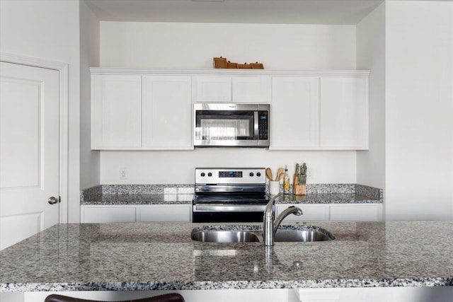 kitchen with a sink, appliances with stainless steel finishes, dark stone countertops, and white cabinetry