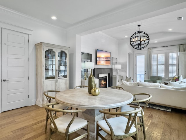 dining space with crown molding, light wood finished floors, a warm lit fireplace, a notable chandelier, and recessed lighting
