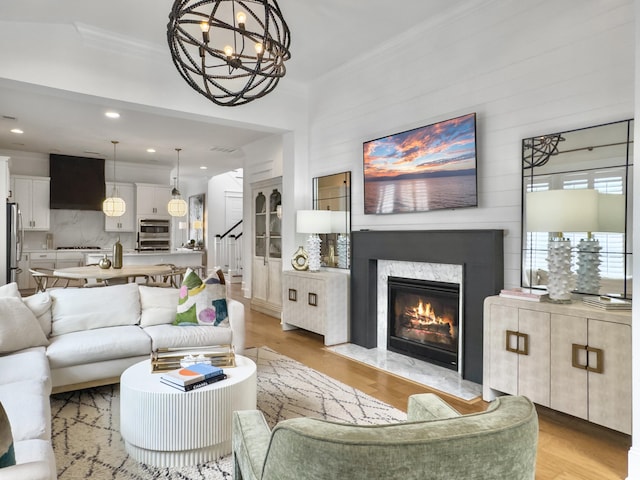 living room featuring light wood-style floors, ornamental molding, a premium fireplace, and a chandelier