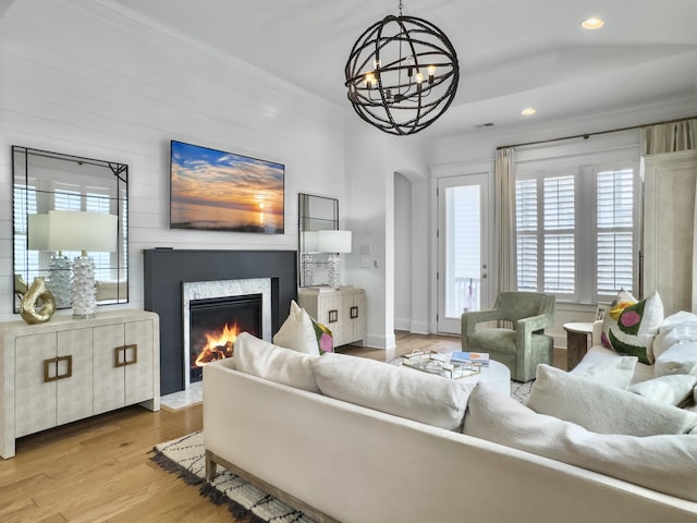 living room with a premium fireplace, arched walkways, a chandelier, wood finished floors, and ornamental molding