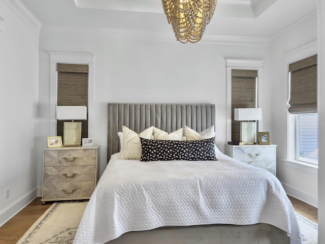 bedroom featuring crown molding, an inviting chandelier, a raised ceiling, baseboards, and wood finished floors