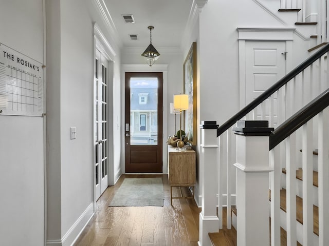 entrance foyer featuring crown molding, light wood-style flooring, stairs, and visible vents