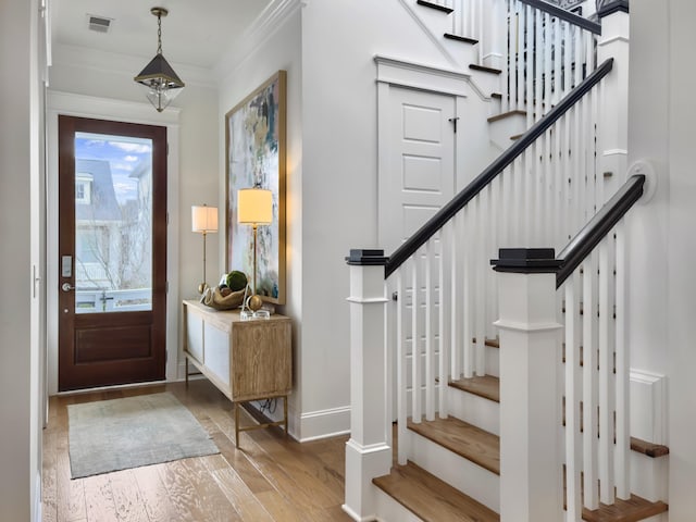 foyer with ornamental molding, wood-type flooring, stairs, and visible vents