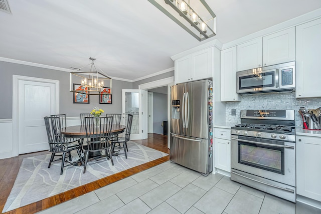 kitchen with crown molding, appliances with stainless steel finishes, white cabinetry, decorative backsplash, and a chandelier