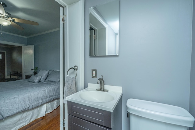 bathroom with toilet, wood-type flooring, ornamental molding, vanity, and ceiling fan