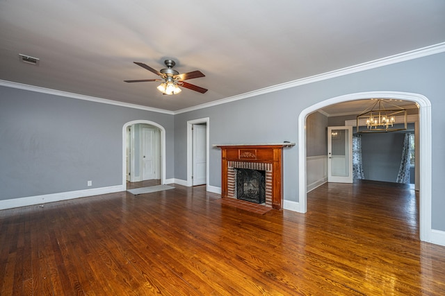 unfurnished living room with crown molding, a brick fireplace, dark wood-type flooring, and ceiling fan with notable chandelier